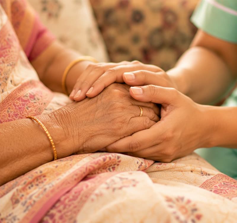 A caregiver gently holding an elderly woman's hands